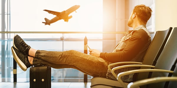 Man at an airport looking out of the window at an aeroplane taking off